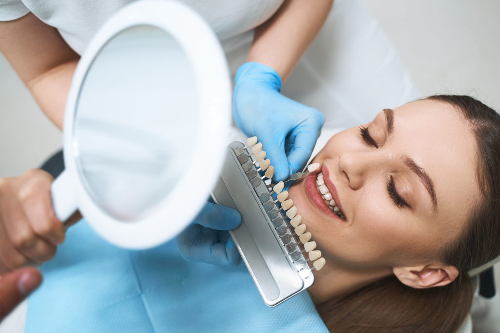 Joyful young female is visiting dentist for choosing veneers and improving her smile with specialist help
